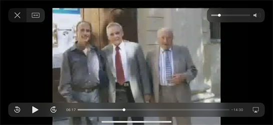 Three men dressed in suits and casual attire are smiling and standing together by a doorway.