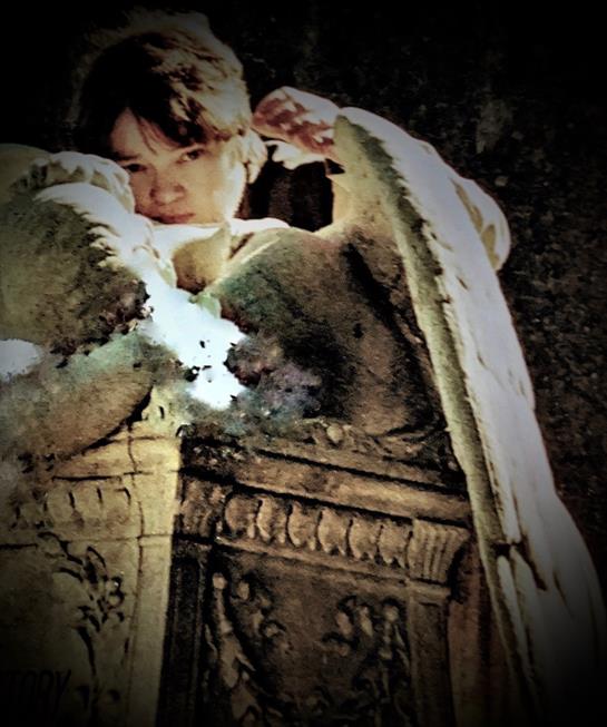 A young person relaxes by a stunning angel sculpture in a tranquil sunset setting.