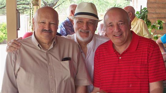 Three friends smile together during a reunion, enjoying the warm sunshine and each other's company.