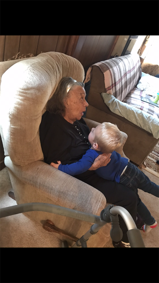 An elderly woman laughs with a young boy as he playfully leans on her in a chair.