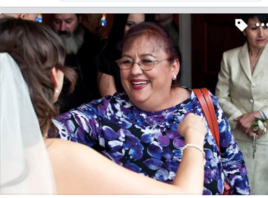 A joyful woman in a floral dress warmly greets a bride during a wedding reception celebration.
