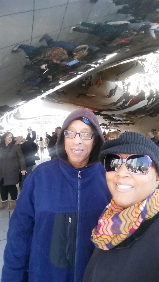 Two friends smile together while visiting a well-known public art piece in an urban park.