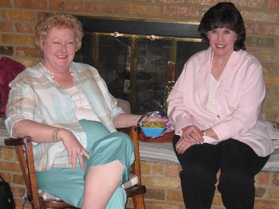 Two friends relax by the fireplace, chatting and enjoying snacks.