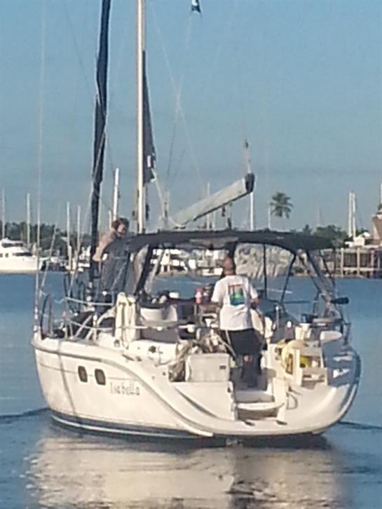 A sailboat navigates through tranquil waters at a marina under sunny skies.