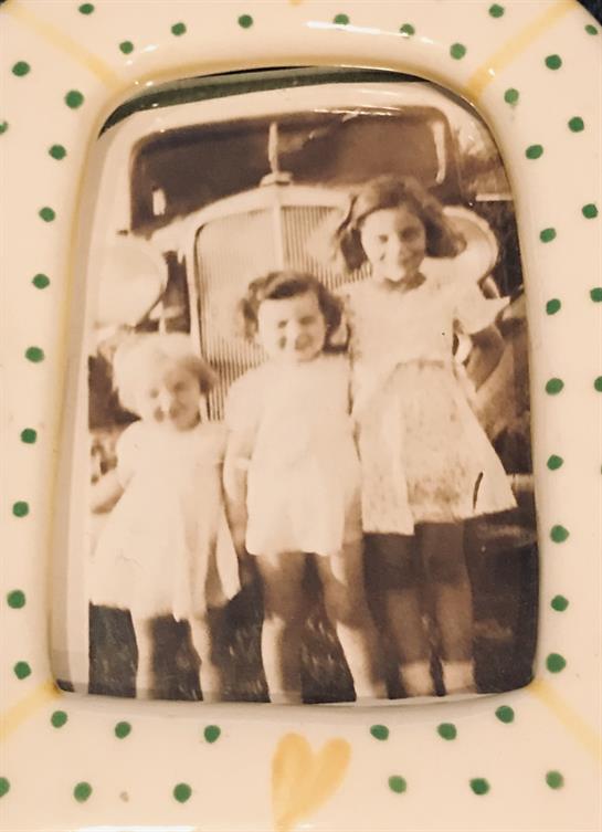 Three girls smile happily in front of an antique truck, capturing a treasured memory.