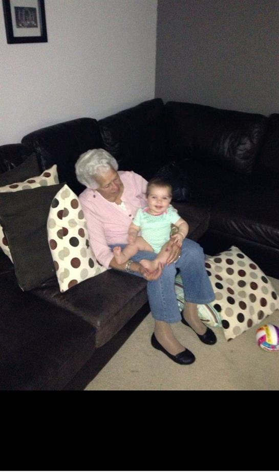 Elderly woman and a baby share a happy moment sitting on a couch surrounded by pillows.