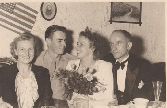 Joyful wedding gathering featuring a bride with flowers, a serviceman, and guests in a cozy room.