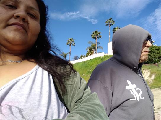 Two friends relax outdoors in a park, surrounded by palm trees under a sunny sky.