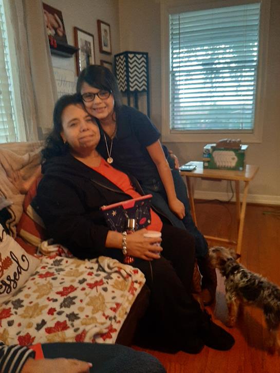 Two women joyfully share a moment in a cozy living room with a playful dog nearby.