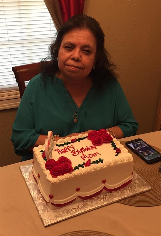 A woman enjoys a birthday celebration with a beautiful cake adorned with flowers and candles.