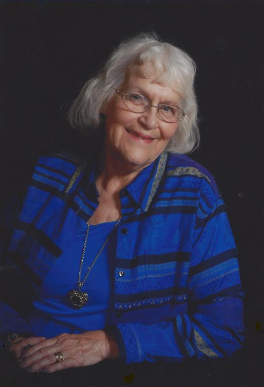 A joyful elderly woman poses wearing a blue and black striped shirt, showcasing her gentle smile.
