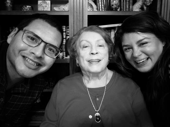Two adults share smiles with their grandmother in a cozy, warm home.