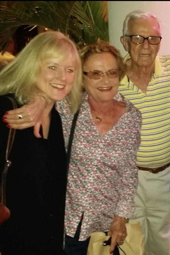 A group of three friends stands together, laughing and enjoying their time at an evening gathering.
