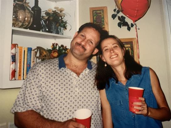 A joyful couple poses together, holding red cups, surrounded by festive decor and smiling.