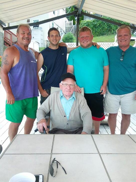 Five relatives smile together outdoors near a lake, enjoying a summer gathering filled with joy.