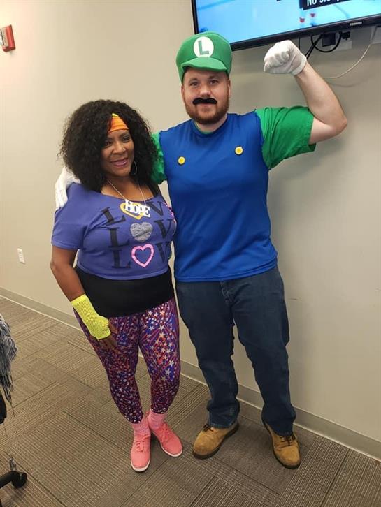 Two friends showcase their vibrant costumes in a cheerful setting at a community gathering.