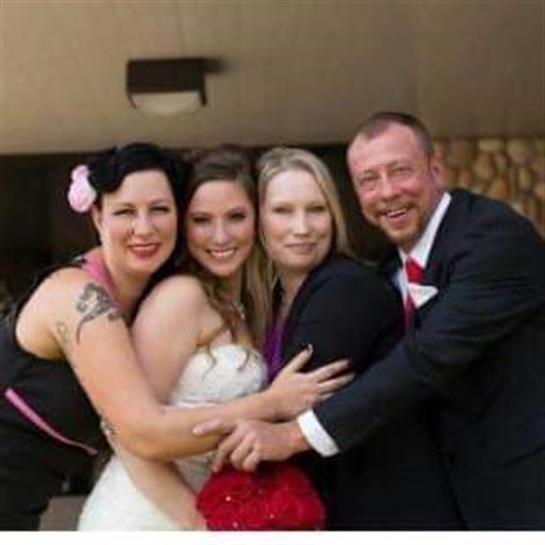 Four friends embrace and smile together at a wedding, celebrating love and friendship in the sun.