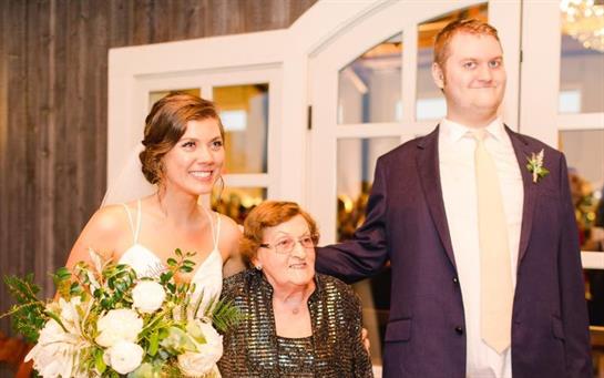 Joyful couple stands with grandmother, celebrating love in a festive atmosphere at a wedding.