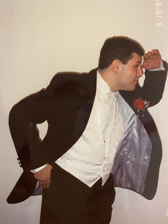 A man dressed in a tuxedo strikes an impressive pose at an indoor gathering, exuding confidence.