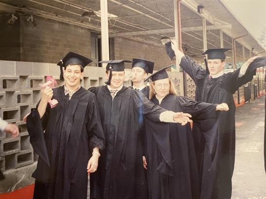 Graduates gather together, smiling and cheering, wearing caps and gowns in a festive atmosphere.