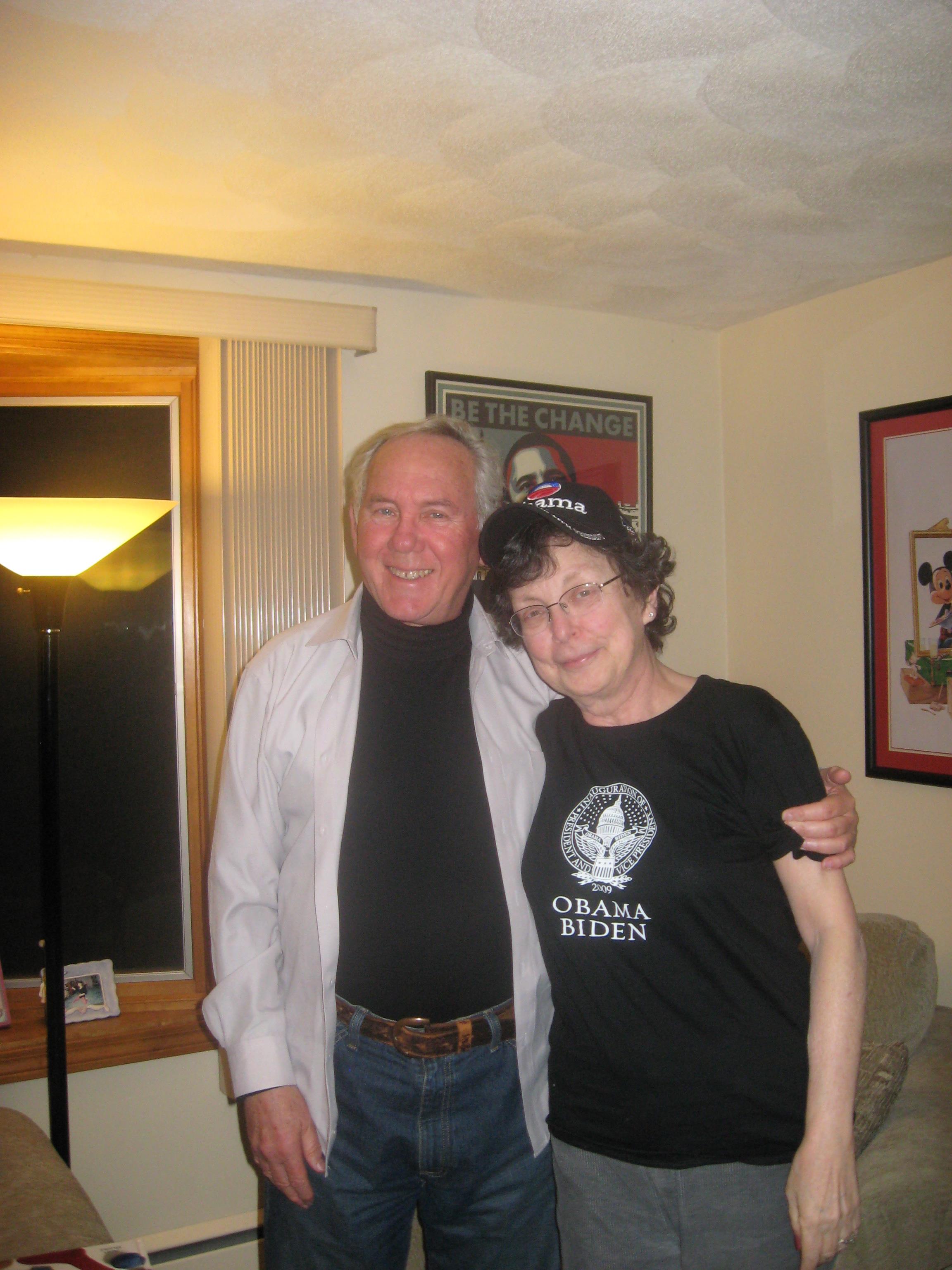 A couple relaxes in their living room, sporting t-shirts and hats to show political support.