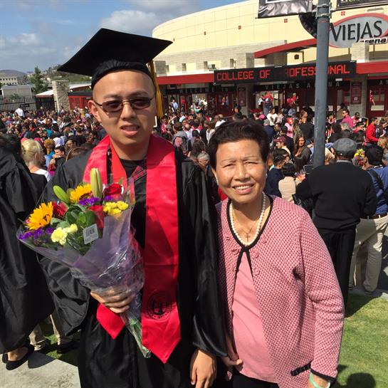 A graduate holds flowers while posing with a family member during a warm day celebration.