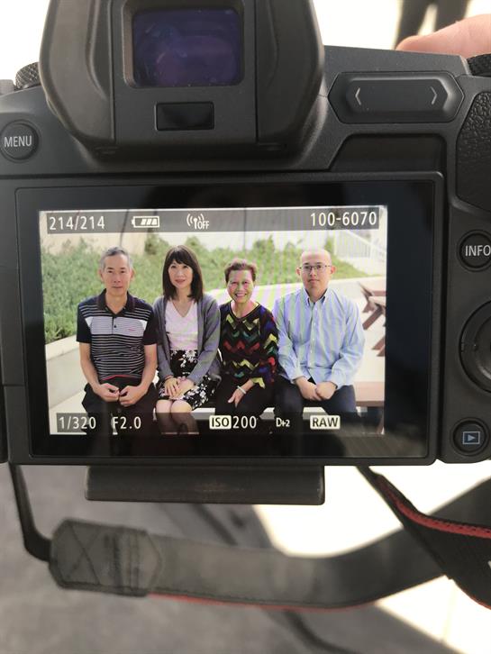 Four friends smile as they gather for a portrait, surrounded by greenery in the park.