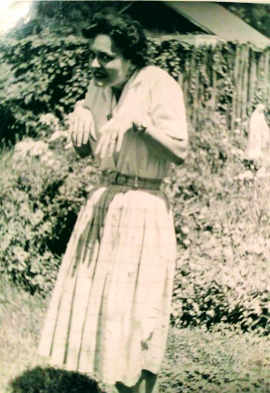 A woman in a long dress is playfully posing in a lush garden, making a humorous expression.