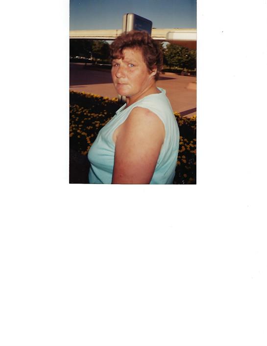 Woman outdoors in a light blue tank top, gazing thoughtfully to the side.