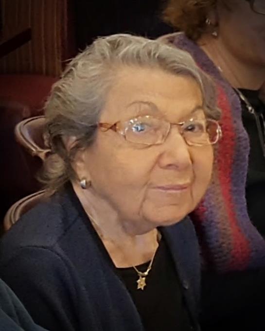 A woman in her eighties sits comfortably with a warm smile, enjoying family time.