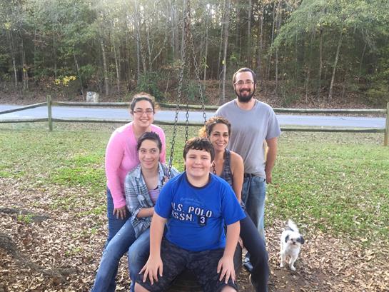 A group of family members poses together in a park, enjoying their time with laughter and a dog.