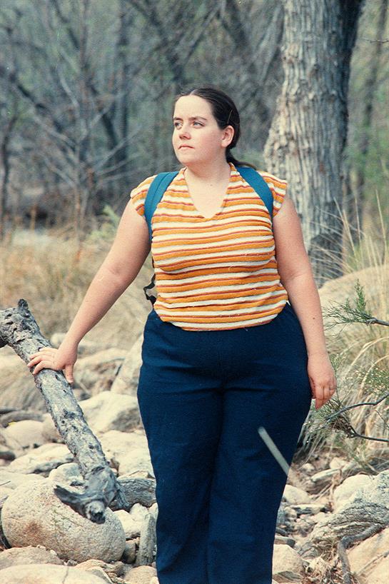 Woman stands near a rocky area, dressed in casual clothing and embracing the outdoors.