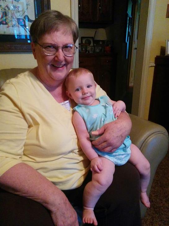 A grandmother sits comfortably on a couch holding her happy granddaughter, sharing a joyful moment.