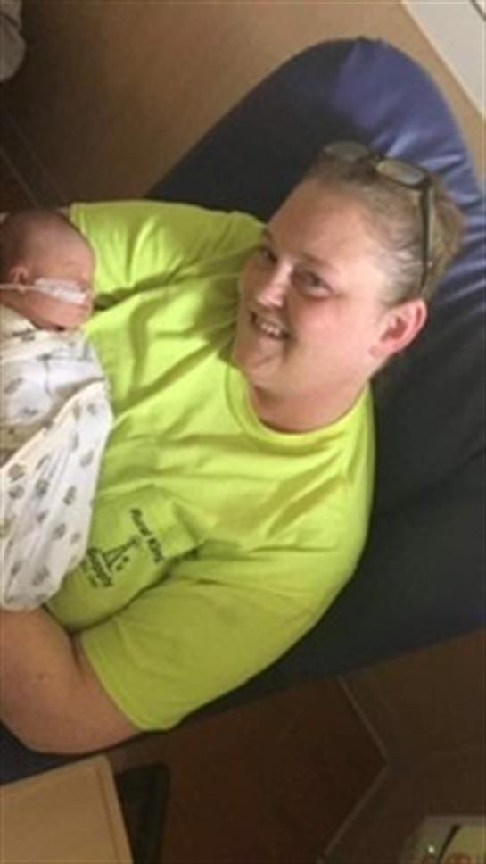 A woman holds a newborn baby gently in a bright and warm indoor space, smiling lovingly.