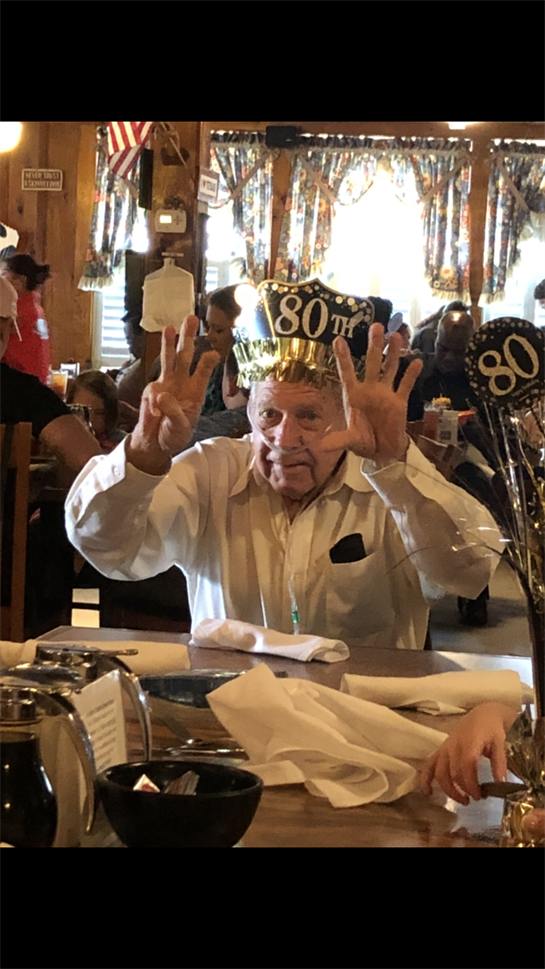 Friends and family gather with excitement to celebrate an elderly man's 80th birthday.