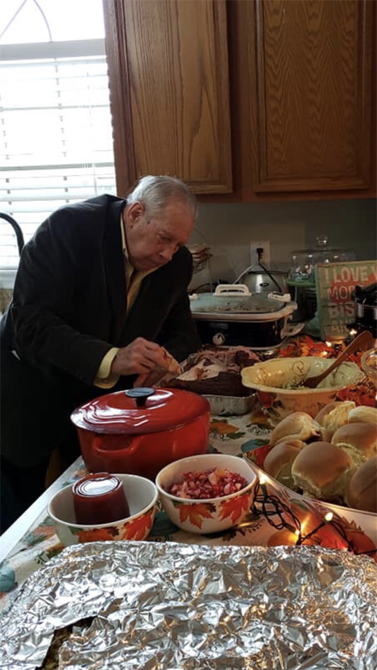 An elderly man serves food at a cozy family gathering adorned with autumn decor.