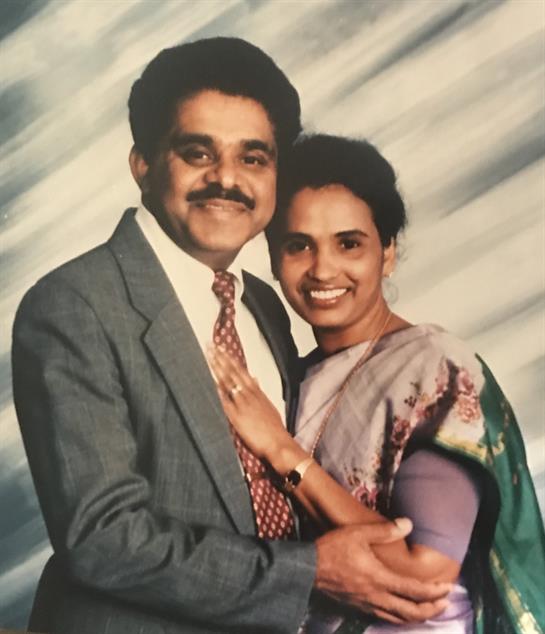 Couple stands close together, smiling warmly while dressed in formal clothing, radiating happiness.