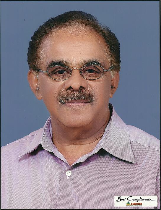 Man with glasses and mustache smiles confidently while wearing a light shirt in a studio setting.