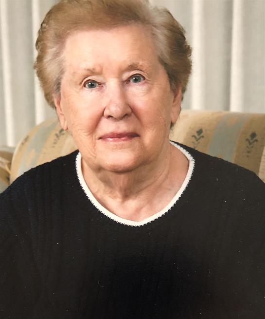 An elderly lady with gray hair sits comfortably, radiating warmth and kindness in her home.