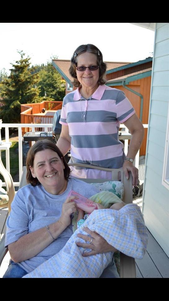 Two women enjoy quality time outside, smiling while holding a baby on a bright sunny day.