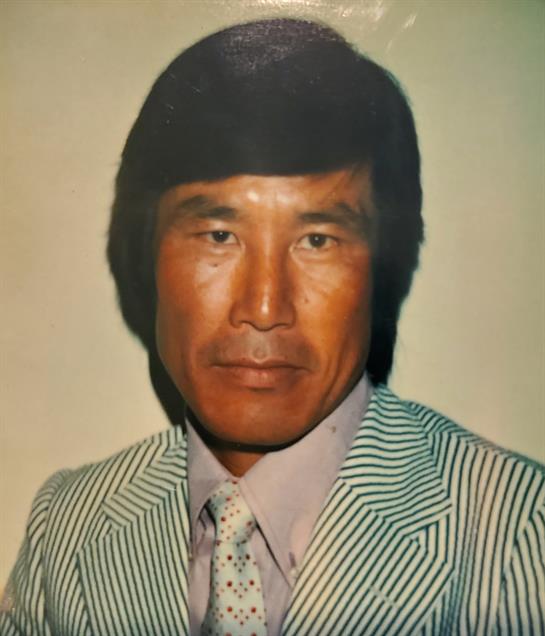 A man with dark hair and a serious expression poses in a striped suit, exuding confidence.