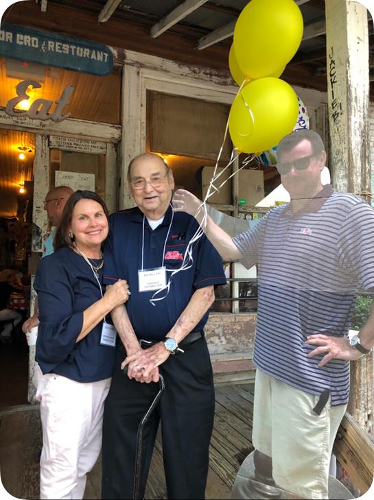 Three people enjoy a cheerful moment together outside a vibrant venue, celebrating with balloons.