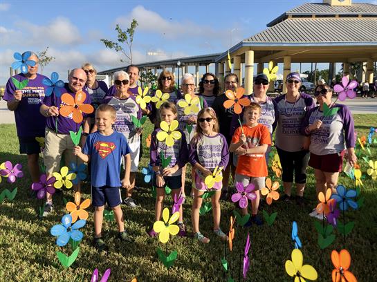 Group of people stands outdoors holding handmade flower decorations in a sunny park environment.