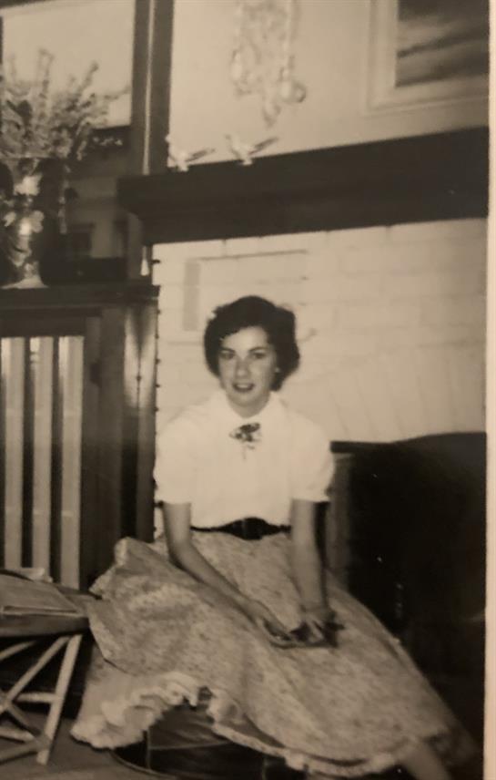 A young woman wearing a classic vintage dress poses with a gentle smile in a cozy interior.