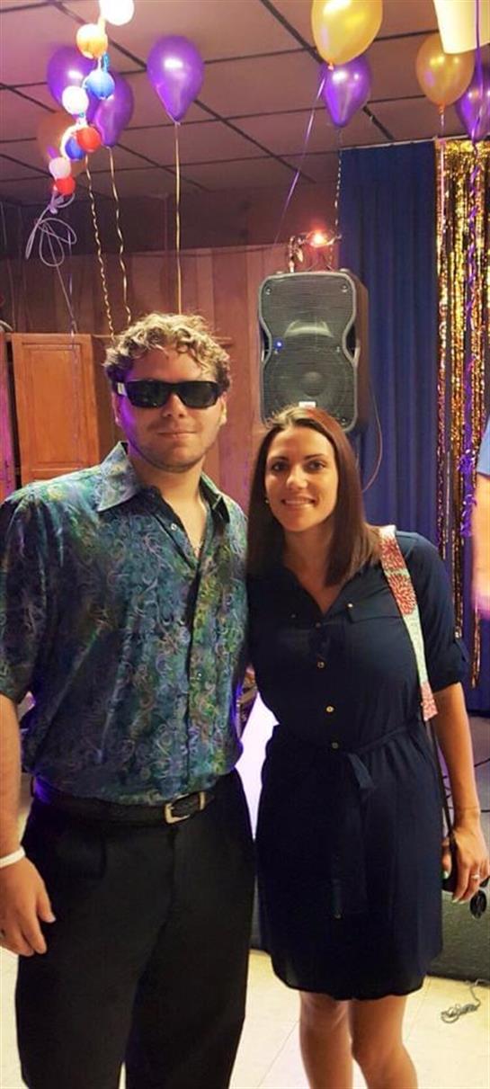 A couple stands smiling together, surrounded by colorful decorations and lights at a festive event.