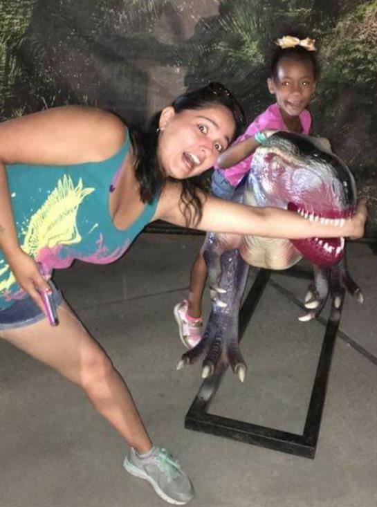 Two children and an adult interact with a dinosaur model, enjoying their time at a park.