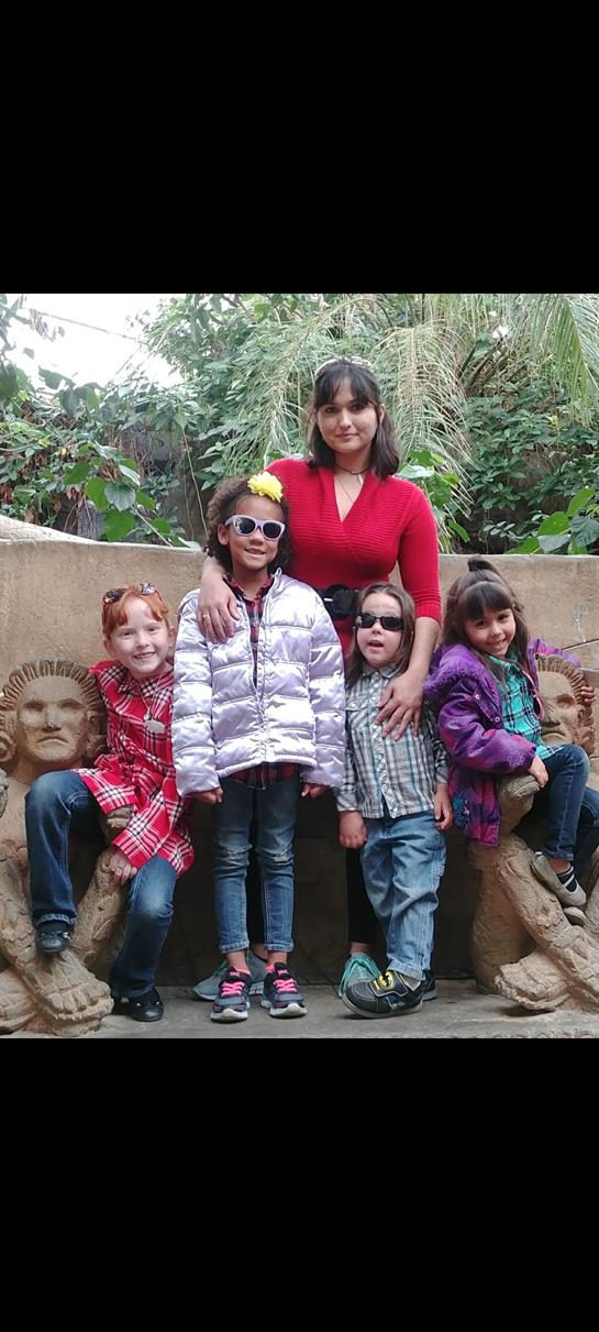 Four children and an adult pose together in a lush garden surrounded by unique sculptures.