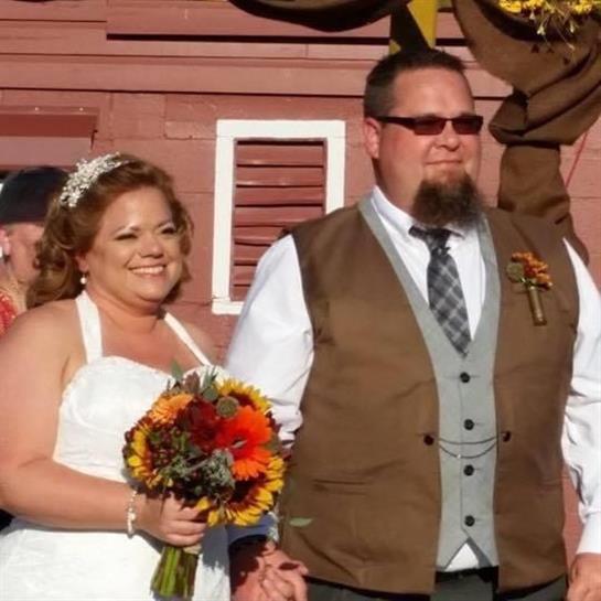 Happy couple in wedding attire holds hands among autumn flowers at sunset.
