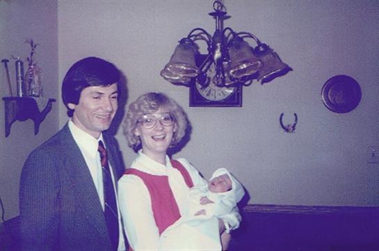 Happy couple smiles as they hold their newborn child in a cozy indoor environment.