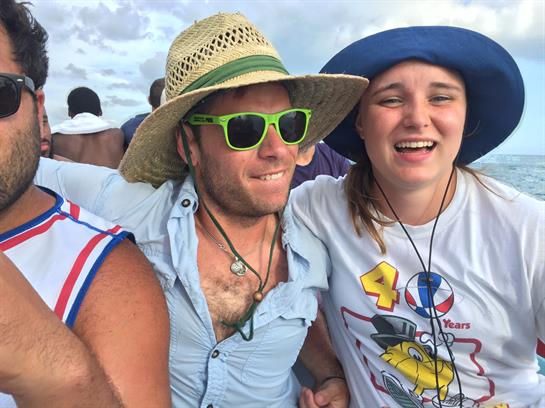 Two friends laugh and celebrate together at a beach party, wearing hats and sunglasses.